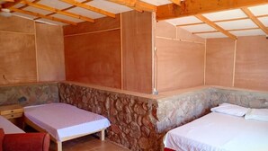 A room with two single beds, a stone wall, wooden beams, and a red chair. - Sahara Beach Camp (Nuweiba)
