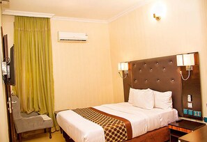 Habitación de hotel con una cama grande, una mesita de noche, una silla, un equipo de aire acondicionado y una cortina verde.