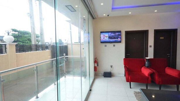 Un moderno vestíbulo de hotel con un separador de vidrio, asientos rojos, un televisor de pantalla plana y un extintor.