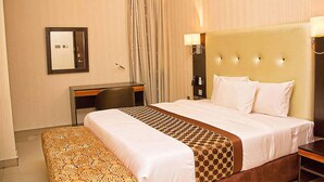 Una habitación de hotel con una cama grande, una mesita de noche, una silla, un escritorio y un espejo.