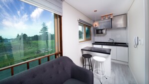 A modern kitchen with a large window, a bar stool, and a grey sofa. - Poeta Pension (Seogwipo)