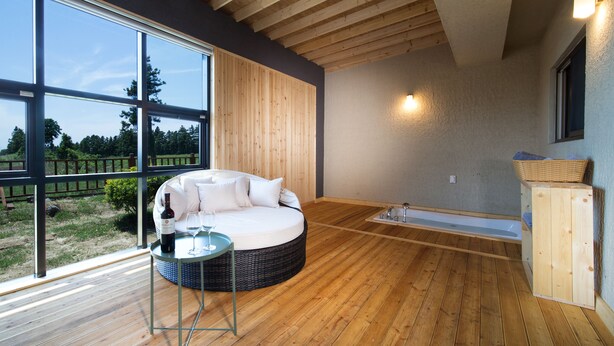 A modern room with a circular sofa, a small table with a bottle and glass, and a wooden floor. - Poeta Pension (Seogwipo)