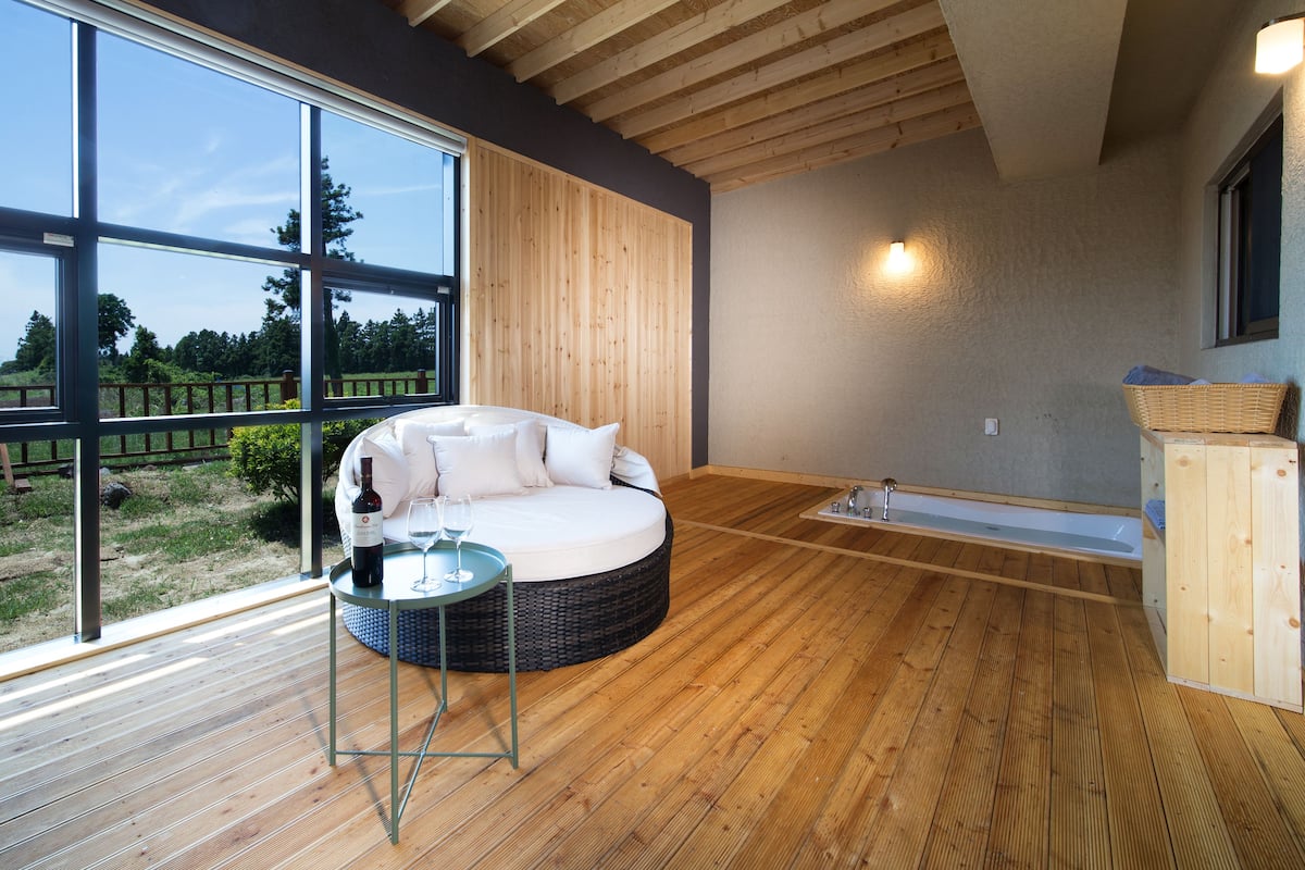A modern room with a circular sofa, a small table with a bottle and glass, and a wooden floor.