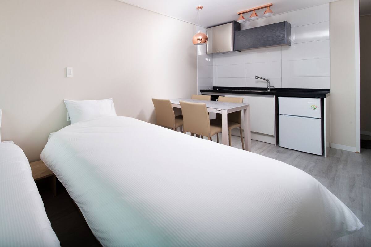 A hotel room with two beds, a small dining table, and a kitchenette.
