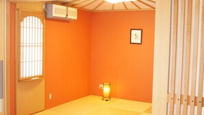 Une pièce aux murs orange, dotée d’un sol recouvert de tatamis, d’une porte coulissante de style shoji et d’un paravent shoji suspendu.