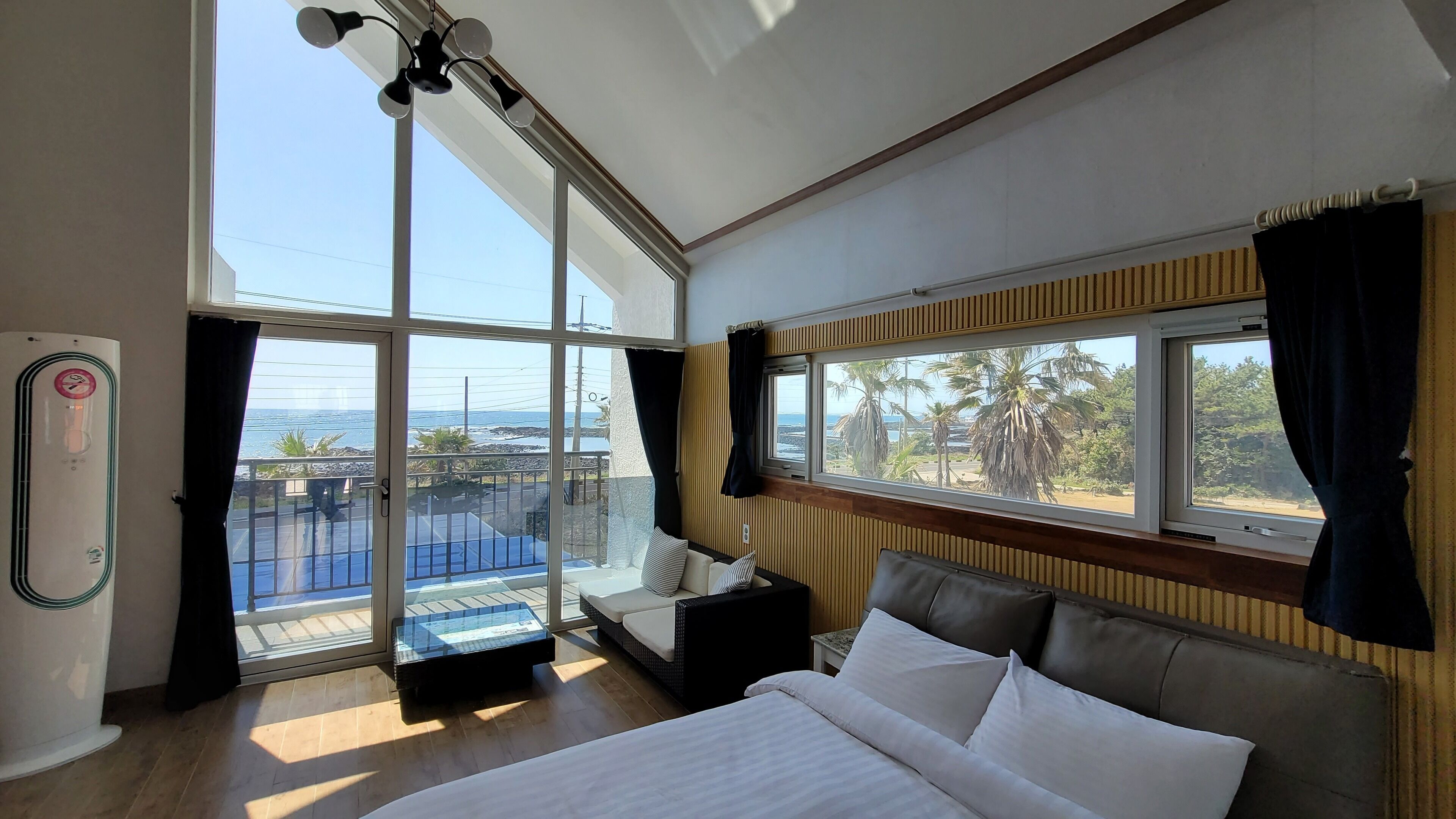 Une chambre d’hôtel moderne dotée d’un grand lit, d’un balcon avec vue sur la mer et d’une grande fenêtre avec des rideaux.