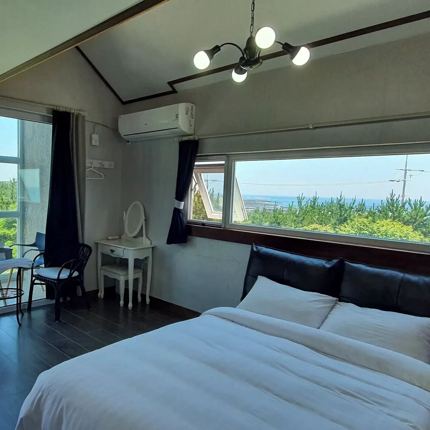 A hotel room with a large bed, a desk with a chair, a window with a view, and an air conditioning unit.