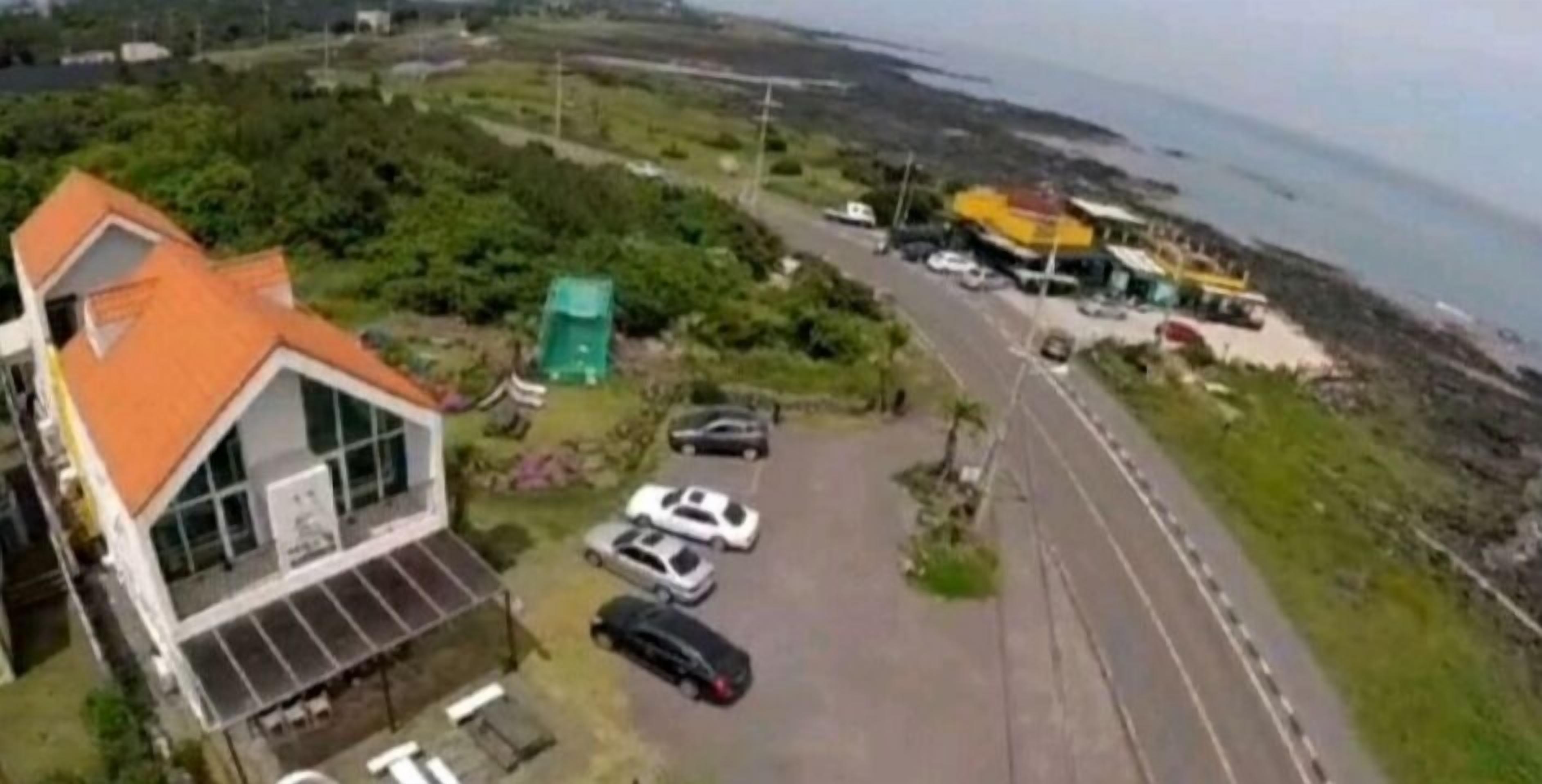 A coastal property with a parking area, a building with a red roof, and a view of the sea.