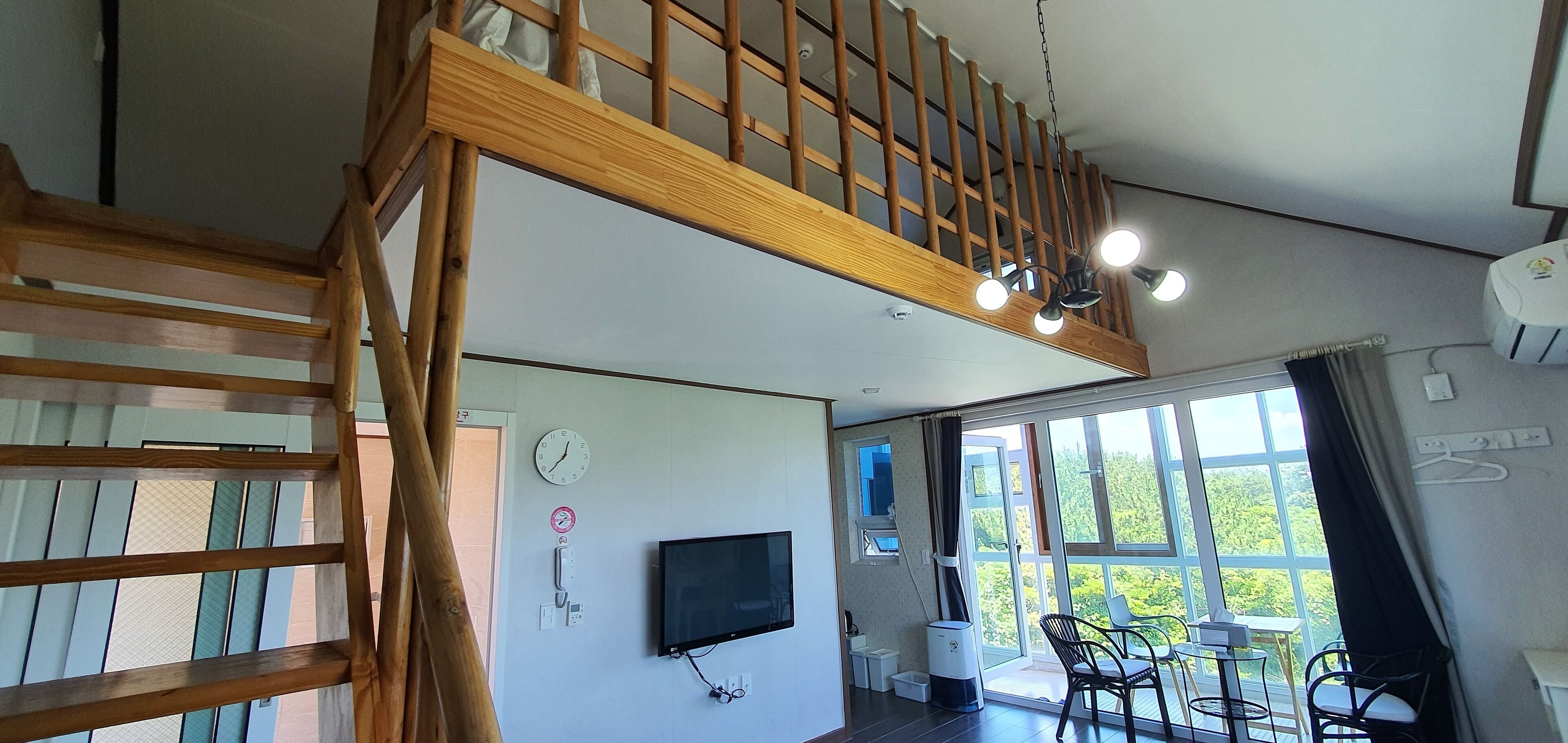 Una habitación amplia con escaleras de madera, televisor de pantalla plana y un balcón con mobiliario exterior.