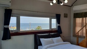 Une chambre à coucher avec un lit, une fenêtre avec des rideaux, un appareil de climatisation et une vue sur la mer.