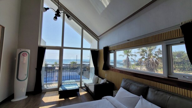 Une chambre d’hôtel dotée d’une grande fenêtre donnant sur l’océan et les palmiers.