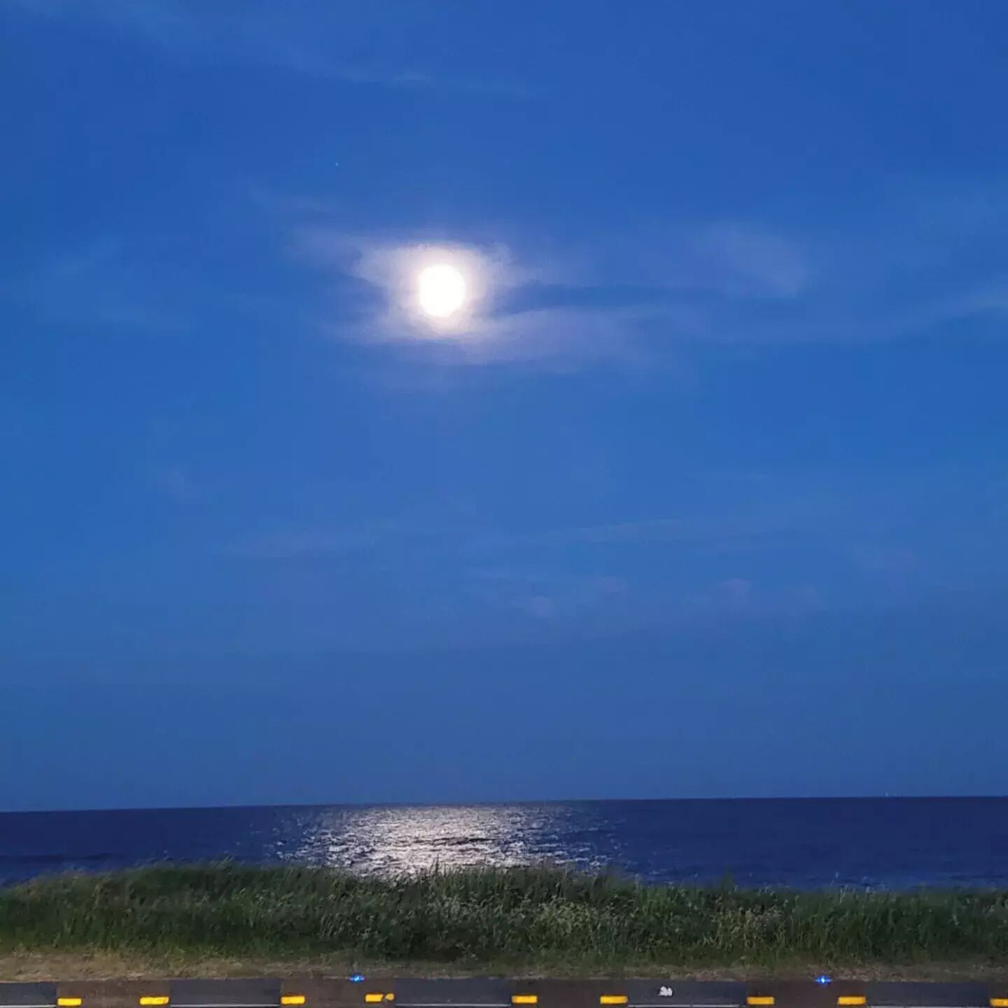 Ein klarer Nachthimmel mit hellem Mond über ruhiger See.
