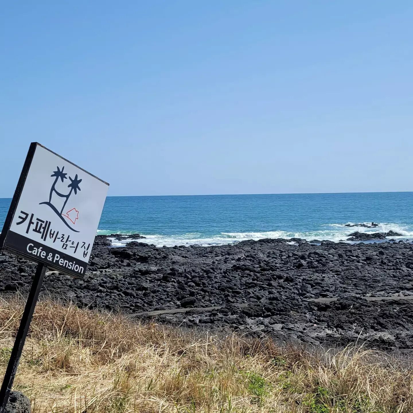 A sign for Cafe & Pension on a rocky beach with the ocean in the background.