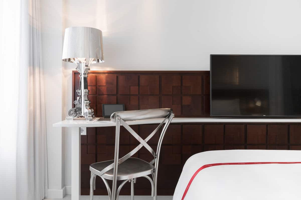 Una habitación de hotel con cama, televisión, escritorio y silla, y una lámpara.