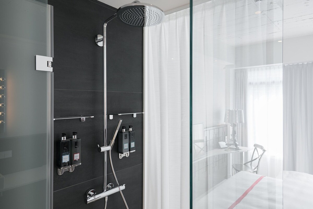 A modern bathroom with a shower, a glass partition, and a bed with a white bedspread.