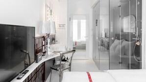 A modern hotel room with a TV, a vanity with mirrors, a shower, and a bed. - Ruby Coco Hotel Dusseldorf by IHG (Düsseldorf)
