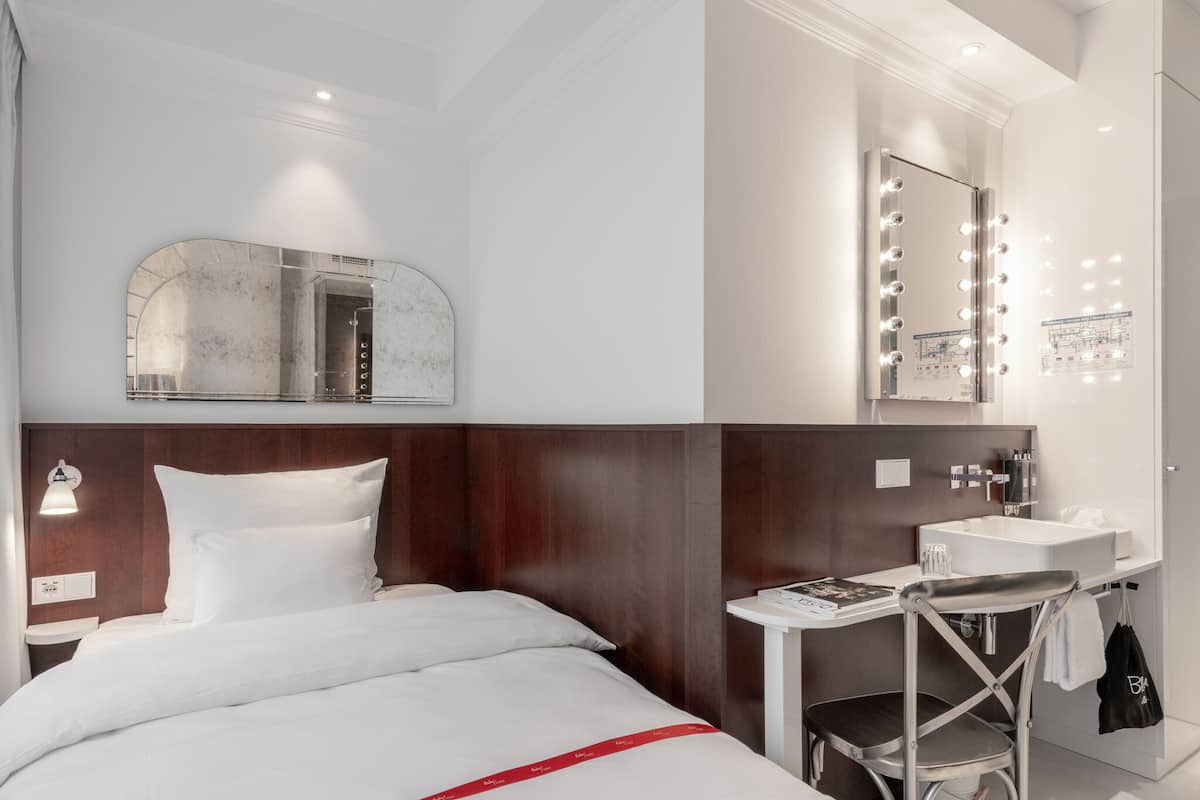 Habitación de hotel con una cama, un tocador con espejo e iluminación, una mesita y una silla.