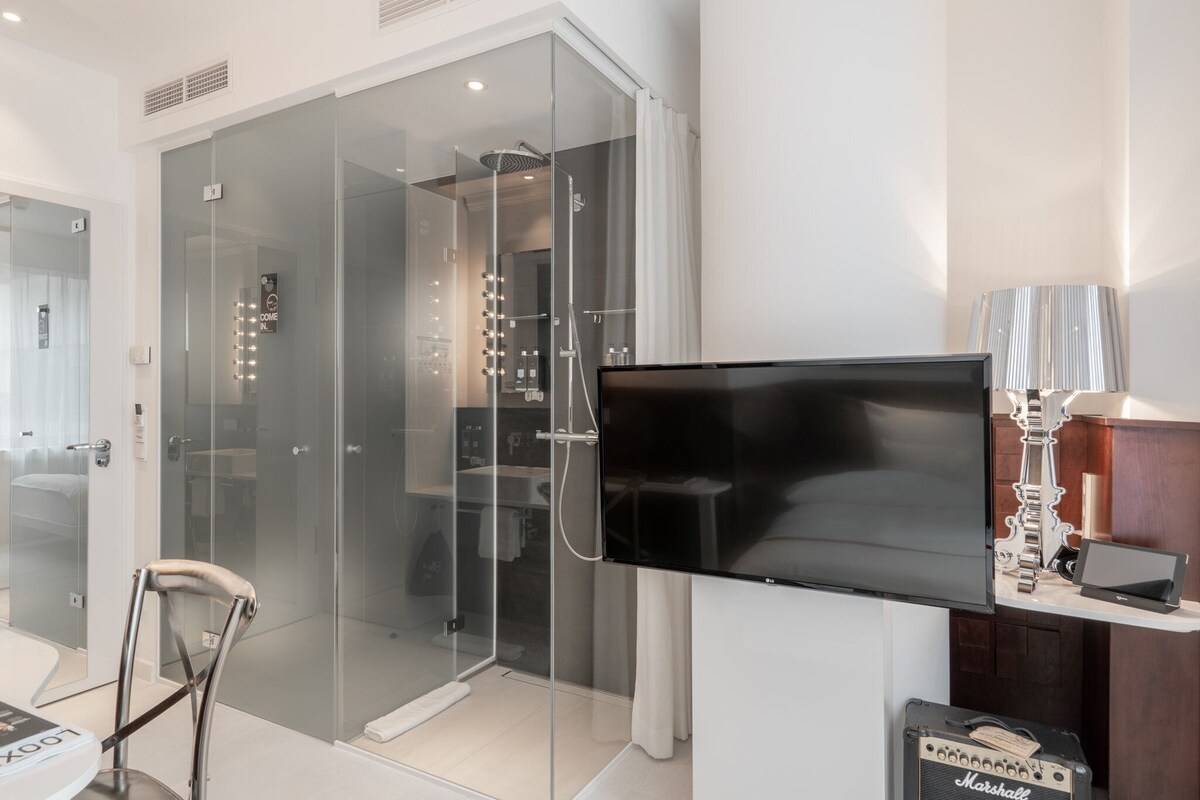 A modern bathroom with a glass-enclosed shower, a mounted television, and a Marshall amplifier.