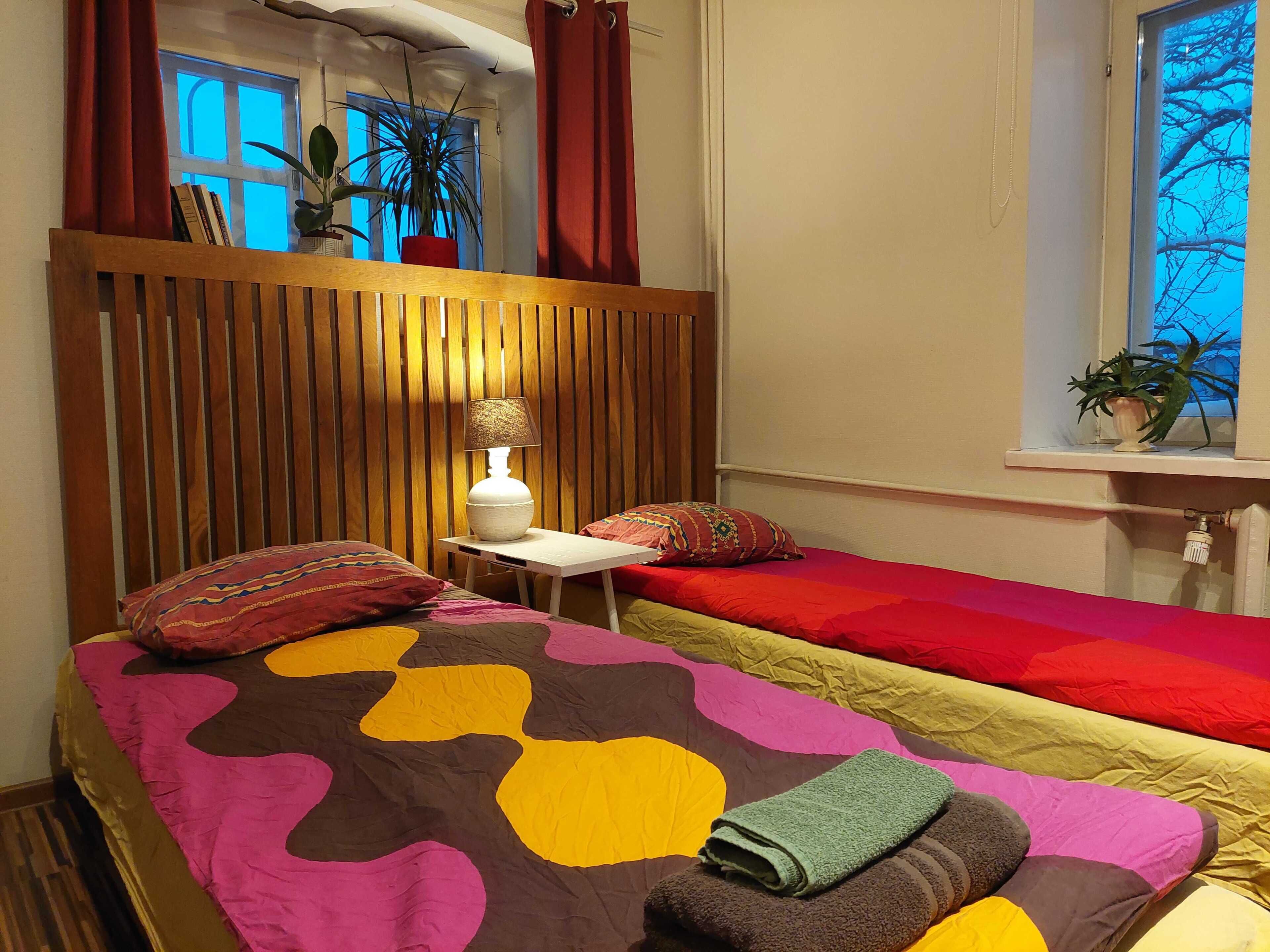 Une chambre avec deux lits, une table de chevet avec une lampe, une fenêtre avec des rideaux et une vue sur les arbres à l’extérieur.