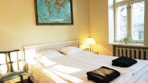 A hotel room with a large bed, a chair, a map on the wall, a window with a plant, and a lamp. - Looming Hostel (Tartu)