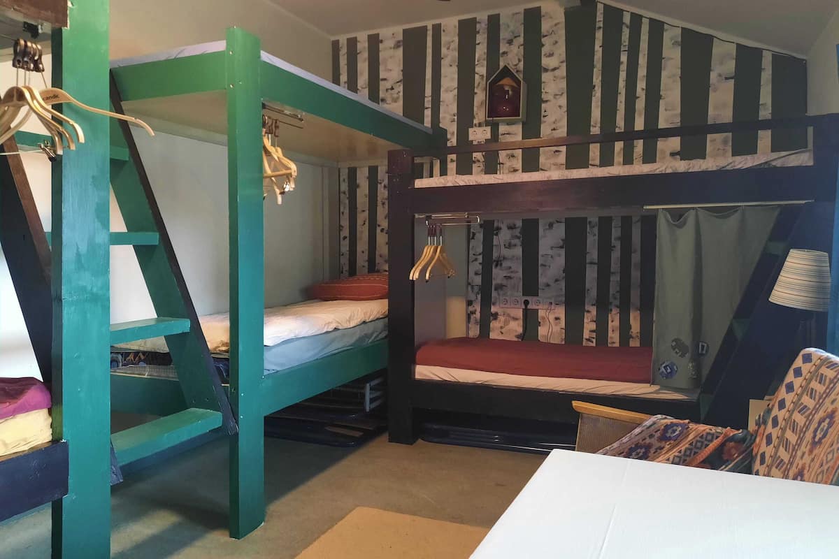 A bunk bed room with striped wallpaper, a small window, and a hanging light fixture.