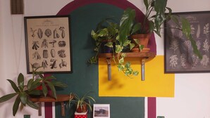 A room with a wooden table, a calendar, a framed botanical illustration, and potted plants on shelves. - Looming Hostel (Tartu)