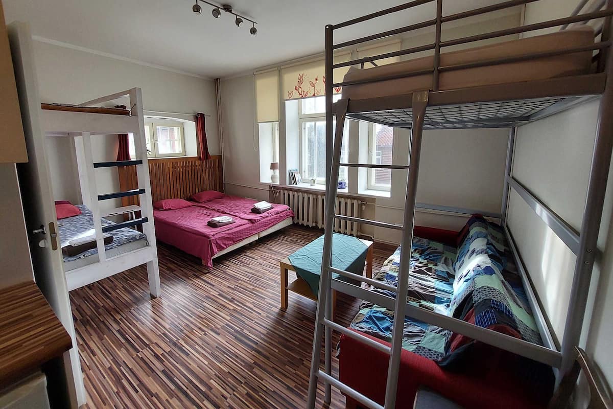 A dormitory room with bunk beds, a wooden floor, a window with curtains, and a radiator.