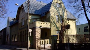 A two-story building with a stone facade, a curved roof, and a small porch with a metal railing. - Looming Hostel (Tartu)