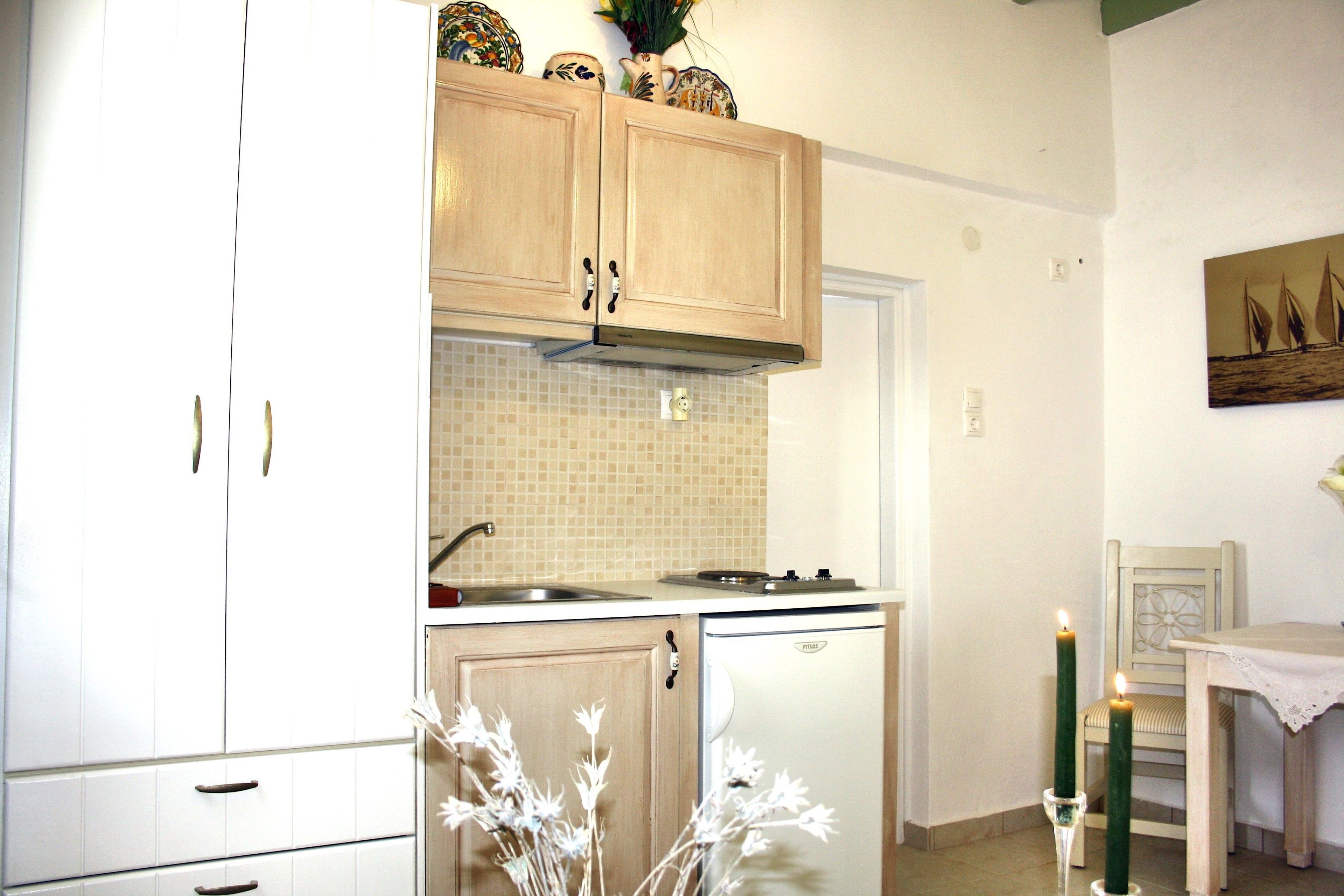 A compact kitchen with white cabinets, a tiled backsplash, a small refrigerator, and a dining area with a table and chairs.