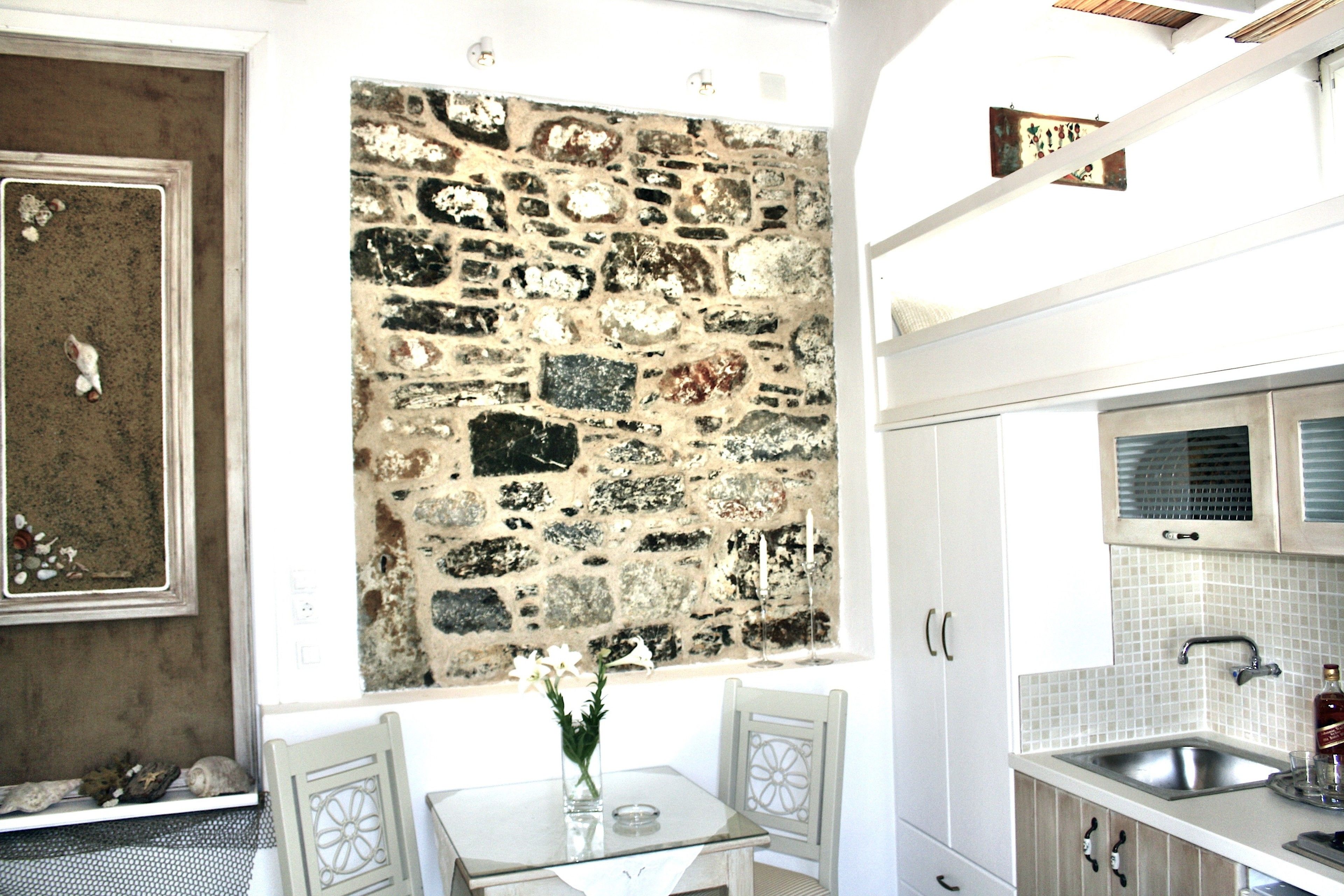 A kitchen with a stone wall, white cabinets, and a tiled backsplash.
