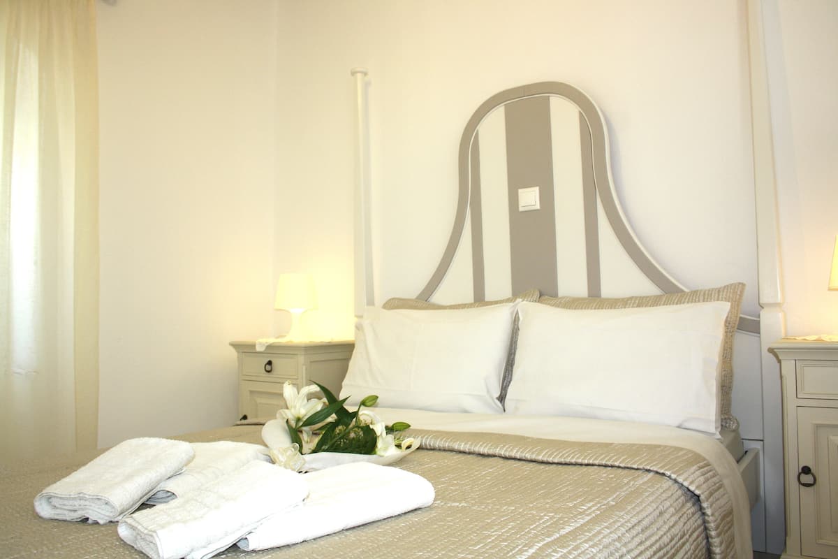 Un lit bien fait, avec du linge de lit blanc et des oreillers, une table de chevet avec une lampe et un petit vase avec des fleurs.