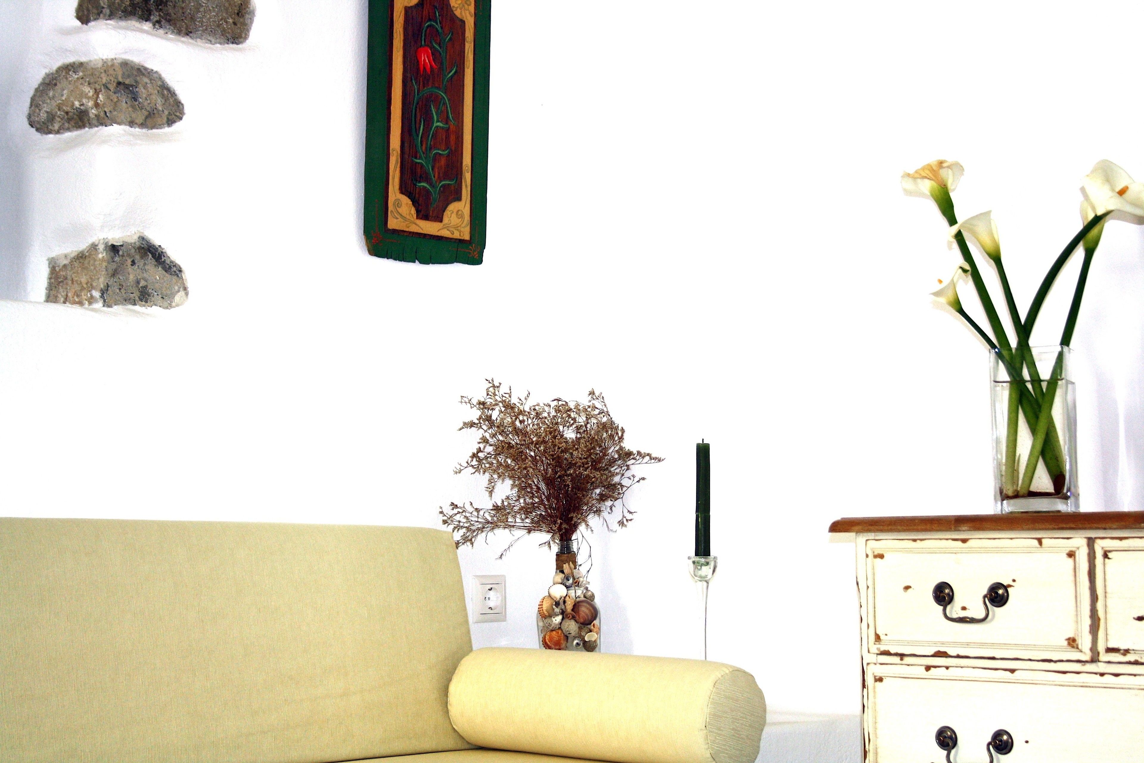 A living room with a sofa, a vase with dried flowers, and a dresser with decorative handles.
