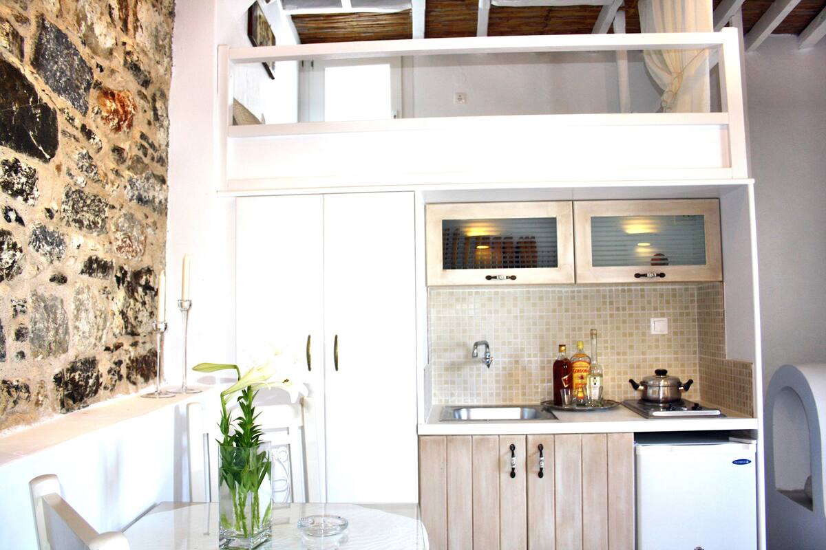 Une cuisine compacte avec un mur en pierre, une table à manger avec des chaises et un petit réfrigérateur.