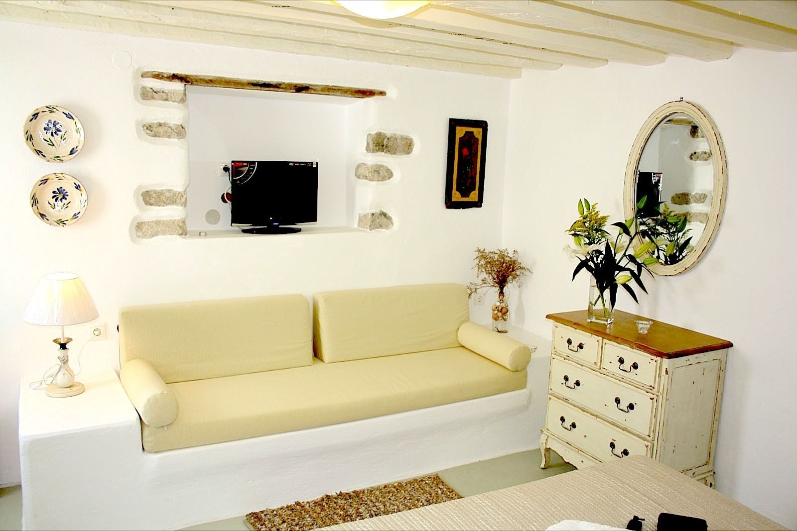 Una habitación con un sofá color beige, un televisor, un espejo y un aparador con cajones.