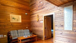 Interior de una cabaña de madera con un sofá, una mesa de centro y una puerta que da a otra habitación.