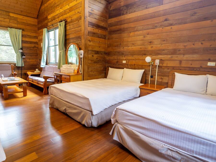Una cabaña con dos camas, un escritorio, una silla y una ventana con cortinas.