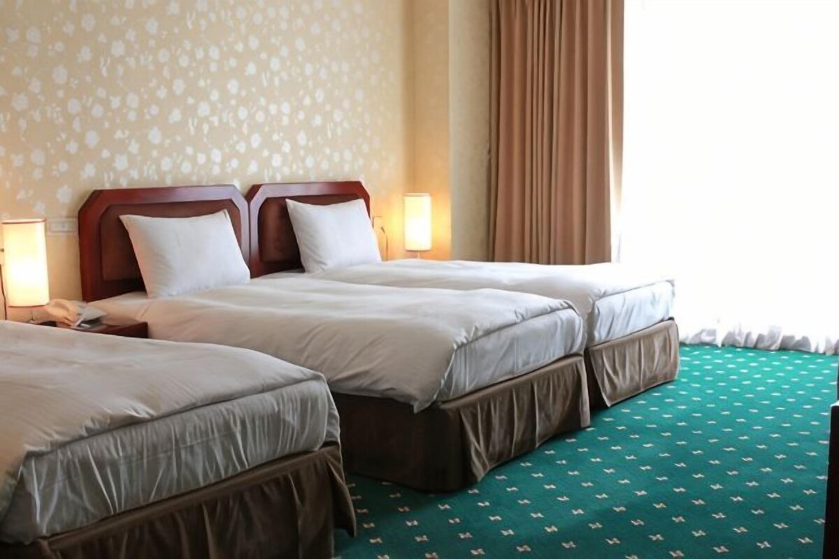 A hotel room with two beds, a patterned wall, and a green carpet.