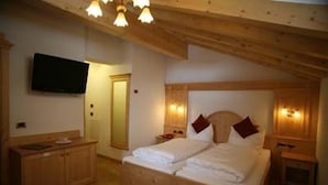 A bedroom with a wooden ceiling, a bed with two pillows, a wooden dresser, and a flat-screen TV mounted on the wall. - Alpen Hotel Vidi (Pinzolo)