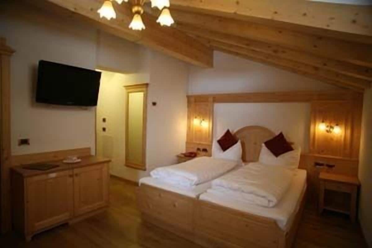 Un dormitorio con techo de madera, una cama con dos almohadas, un aparador de madera y un televisor de pantalla plana montado en la pared.