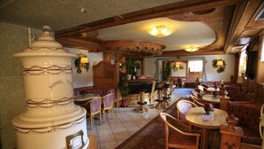 A hotel lobby with a large decorative urn, wooden furniture, and a patterned rug. - Alpen Hotel Vidi (Pinzolo)