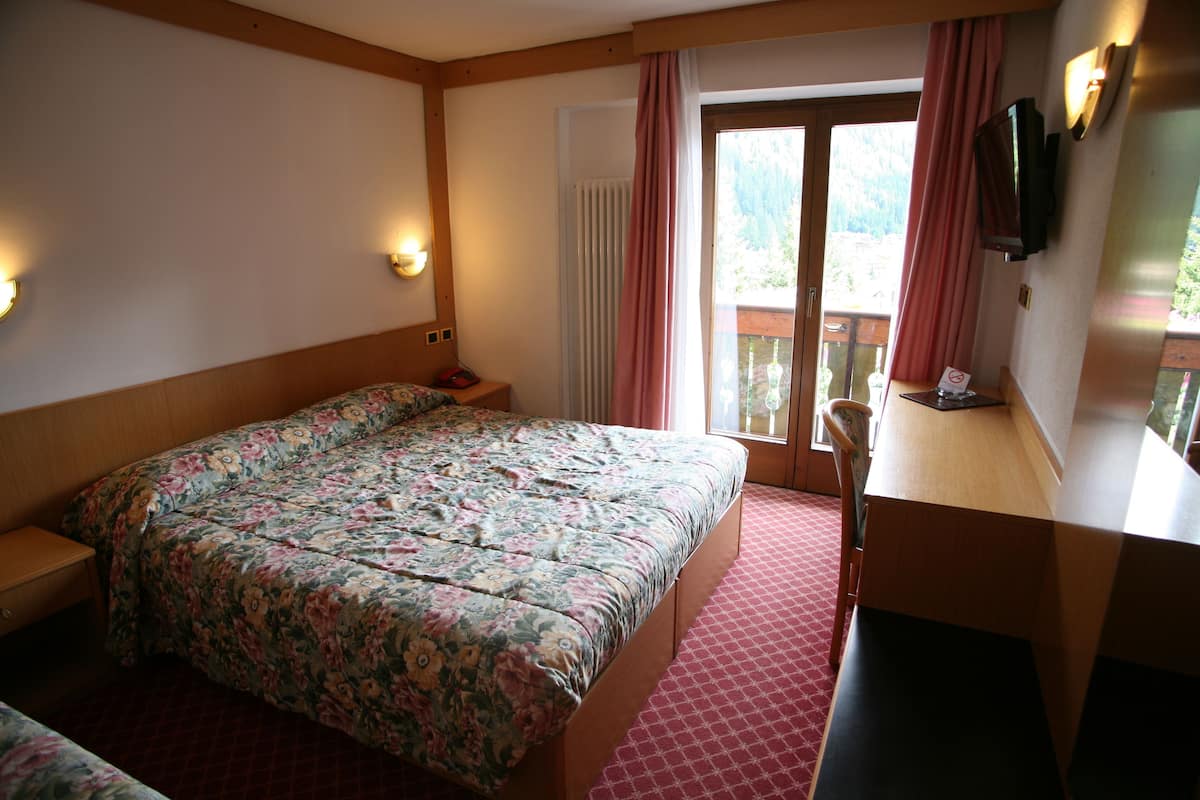 Habitación de hotel con una cama grande, un escritorio, una silla, un televisor y un balcón con cortinas.