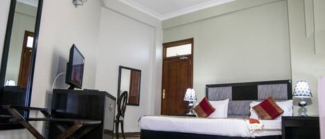A hotel room with a bed, bedside tables, a TV, a desk, and a chair.