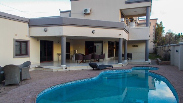 Una moderna casa a due piani con piscina, mobili da esterno e una veranda coperta.