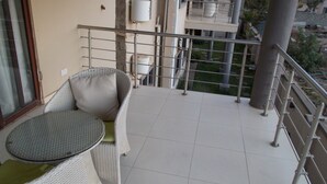 Un balcone con una sedia e un tavolino in vimini, un corrimano in metallo e vista su un edificio sullo sfondo.