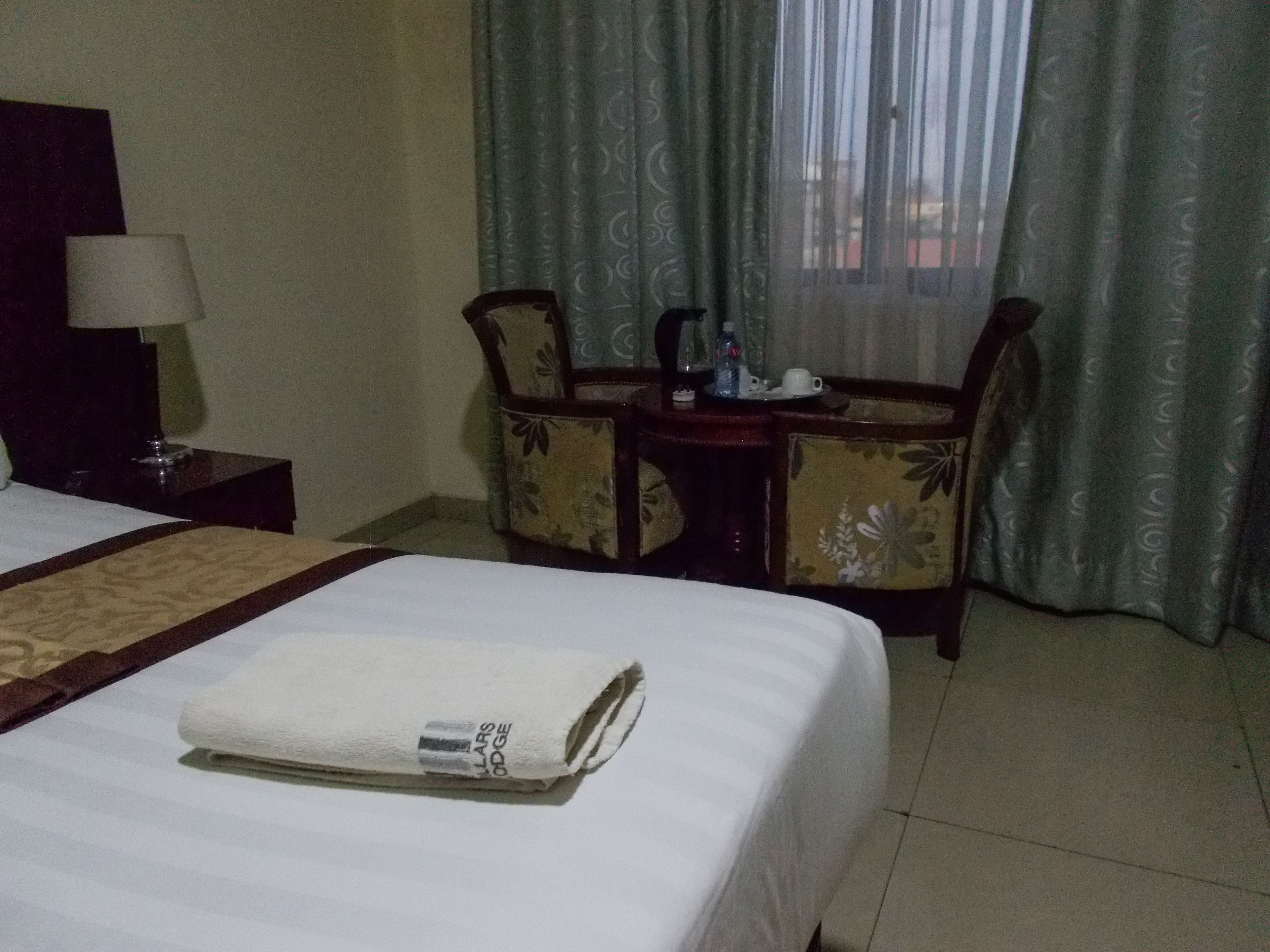 Una habitación de hotel con una cama bien hecha, una mesita con una lámpara y una silla.