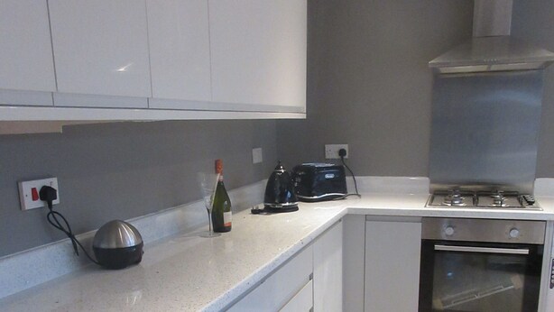 A modern kitchen with white cabinets, a built-in oven, and a countertop with a kettle and a bottle of wine. - Magdala House (Liverpool)