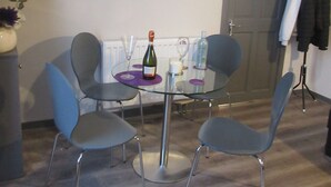 A dining area with a glass table, four grey chairs, a bottle of wine, and a painting on the wall. - Magdala House (Liverpool)