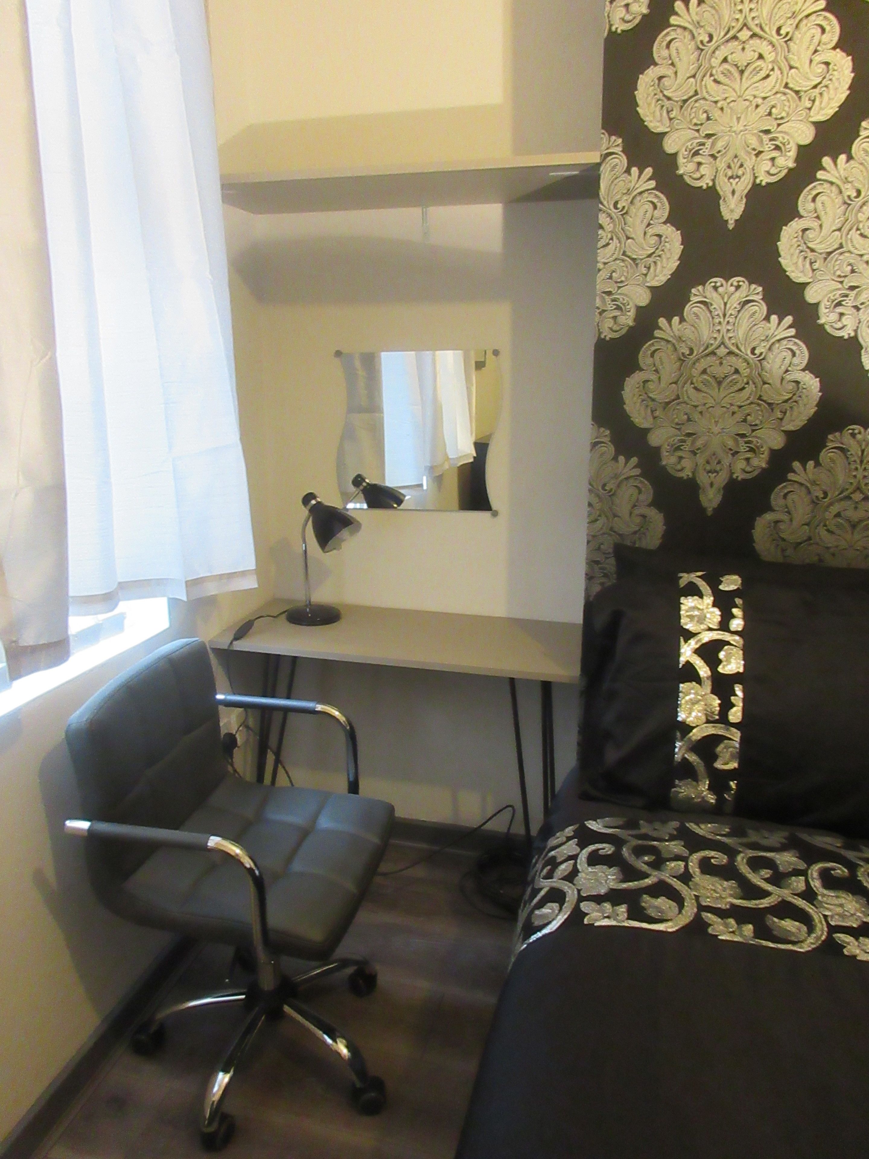A compact hotel room with a desk, chair, and a bed with patterned bedding.