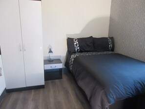 A bedroom with a bed, a wardrobe, a nightstand, and a lamp.
