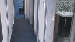 A narrow hallway with a carpeted floor leading to a bathroom with a tiled backsplash and a sink. - Magdala House (Liverpool)